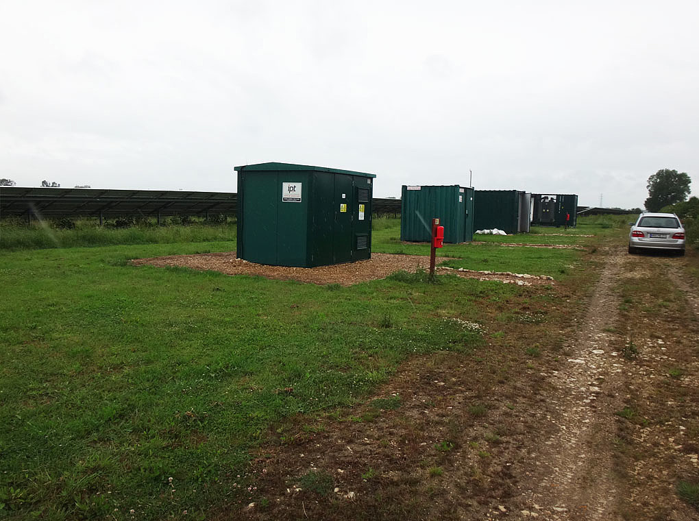 The picture shows the entrance to the PV farm Folly with CCTV, storage container, substation and a central inverter.